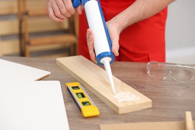 Photo of Worker with caulking gun glueing wooden plank indoors, closeup