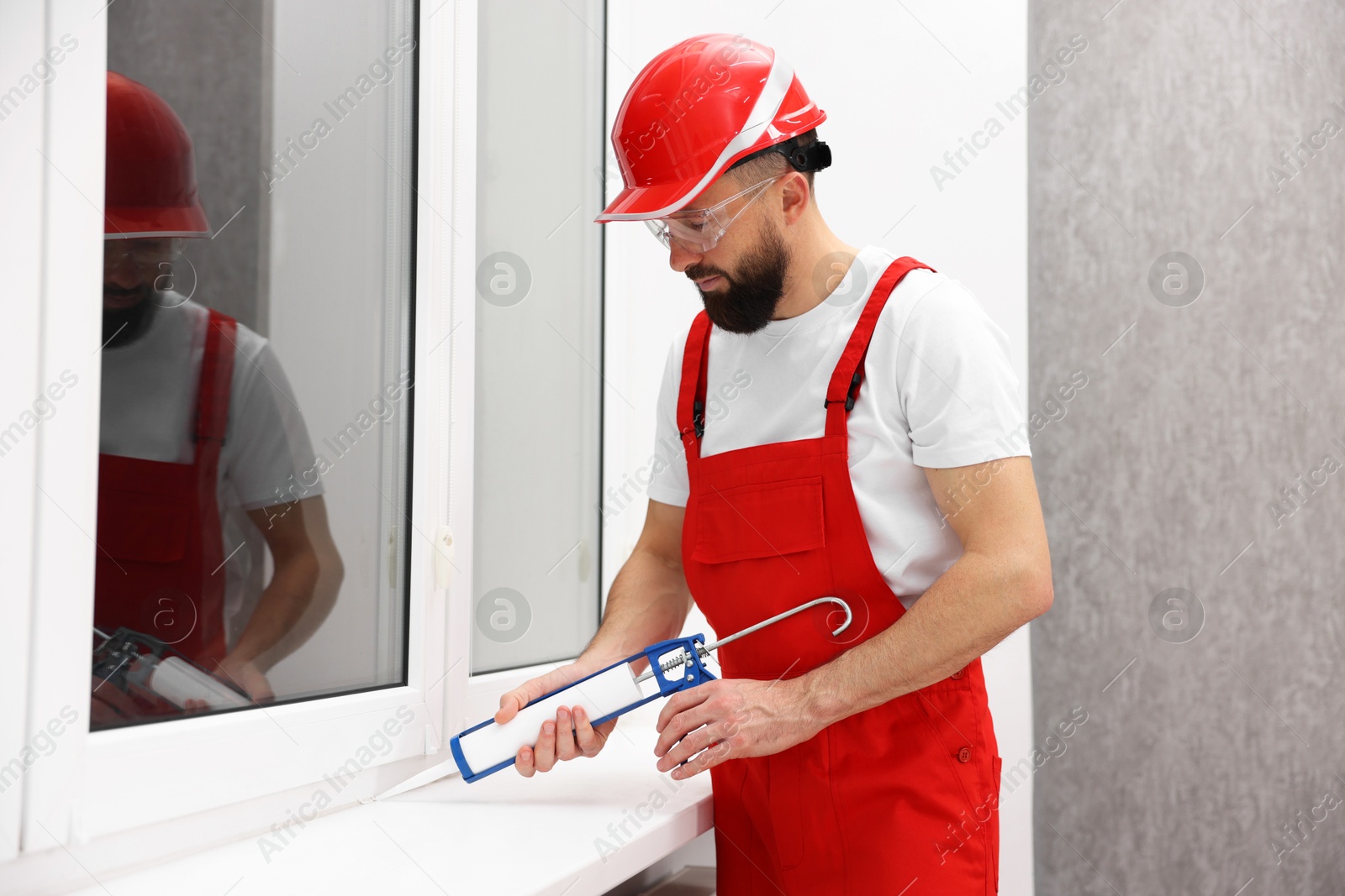 Photo of Worker with caulking gun sealing window indoors