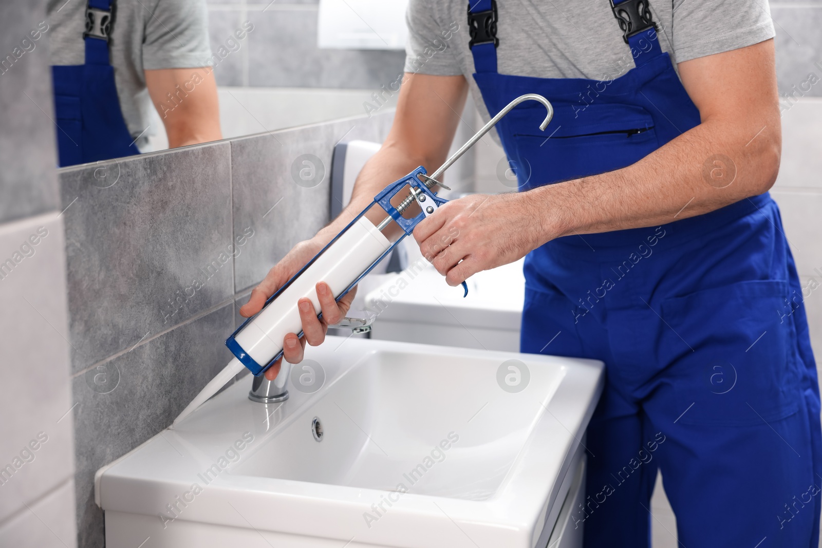 Photo of Worker with caulking gun sealing washbasin in bathroom, closeup