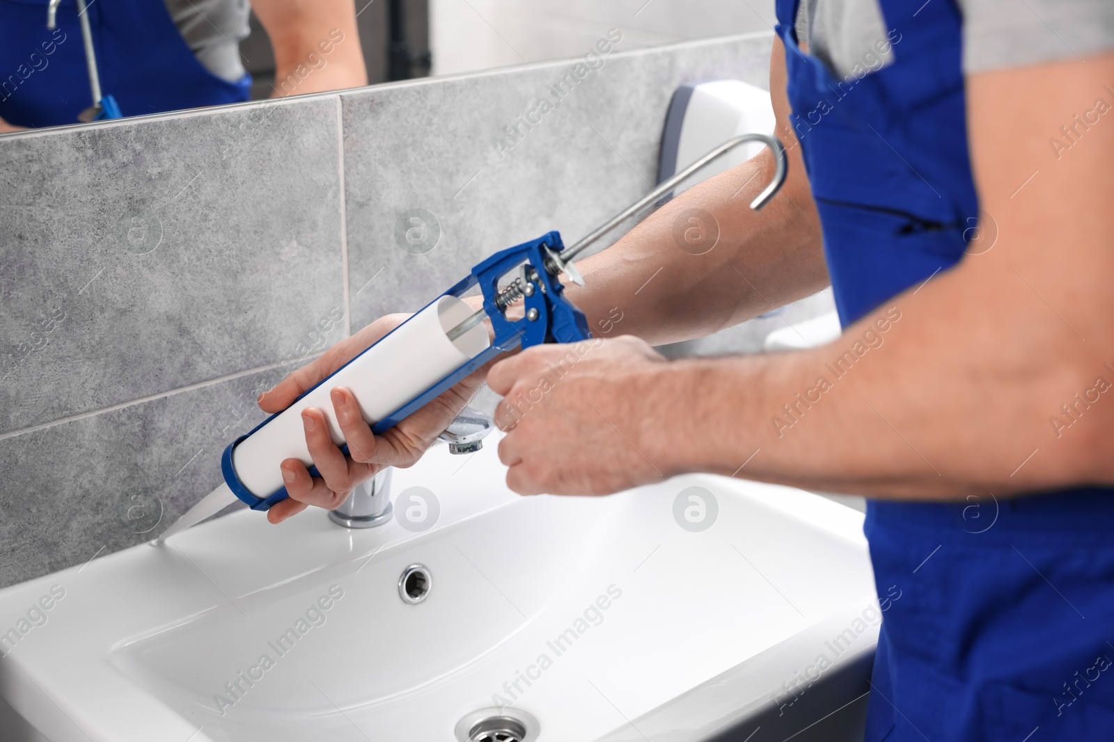 Photo of Worker with caulking gun sealing washbasin in bathroom, closeup