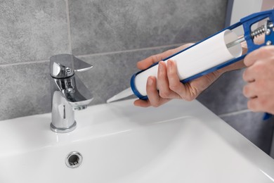 Photo of Man with caulking gun sealing washbasin in bathroom, closeup