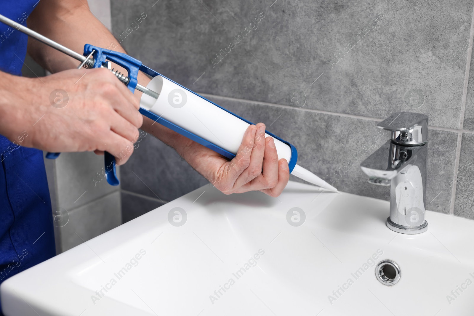 Photo of Man with caulking gun sealing washbasin in bathroom, closeup