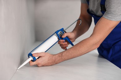 Photo of Worker with caulking gun sealing countertop indoors, closeup