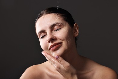 Photo of Attractive woman washing her face on black background, closeup