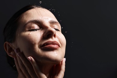 Photo of Attractive woman washing her face on black background, closeup. Space for text