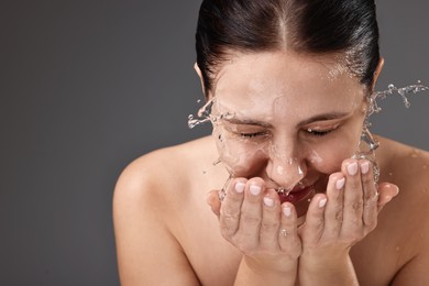 Photo of Woman washing her face on grey background, space for text