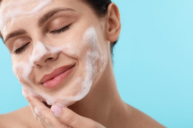 Photo of Attractive woman washing her face with cleansing foam on light blue background, closeup. Space for text