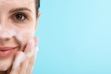 Photo of Attractive woman washing her face with cleansing foam on light blue background, closeup. Space for text