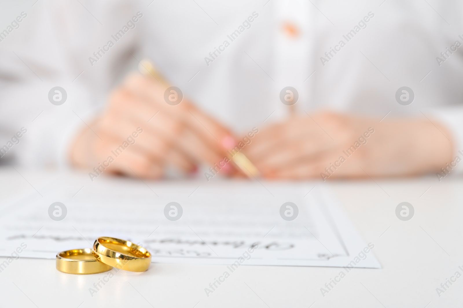 Photo of Woman signing marriage contract and wedding rings on desk, selective focus