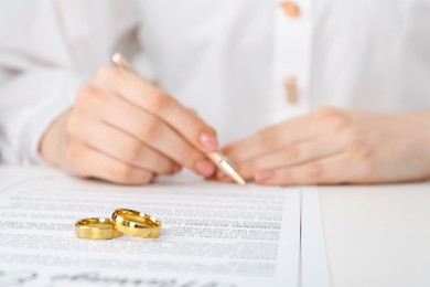 Photo of Woman signing marriage contract and wedding rings on desk, selective focus