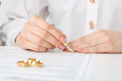 Photo of Woman signing marriage contract and wedding rings on desk, selective focus