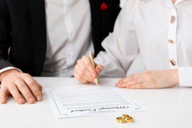 Photo of Newlyweds signing marriage contract and wedding rings on desk, selective focus