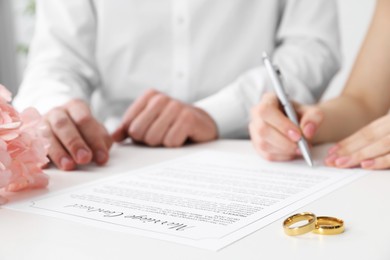 Photo of Newlyweds signing marriage contract and wedding rings on desk, selective focus