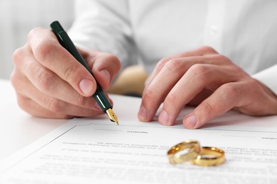 Photo of Man signing marriage contract and wedding rings on desk, selective focus