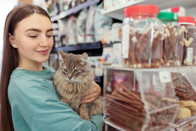 Photo of Woman choosing treats for her cute cat in pet shop