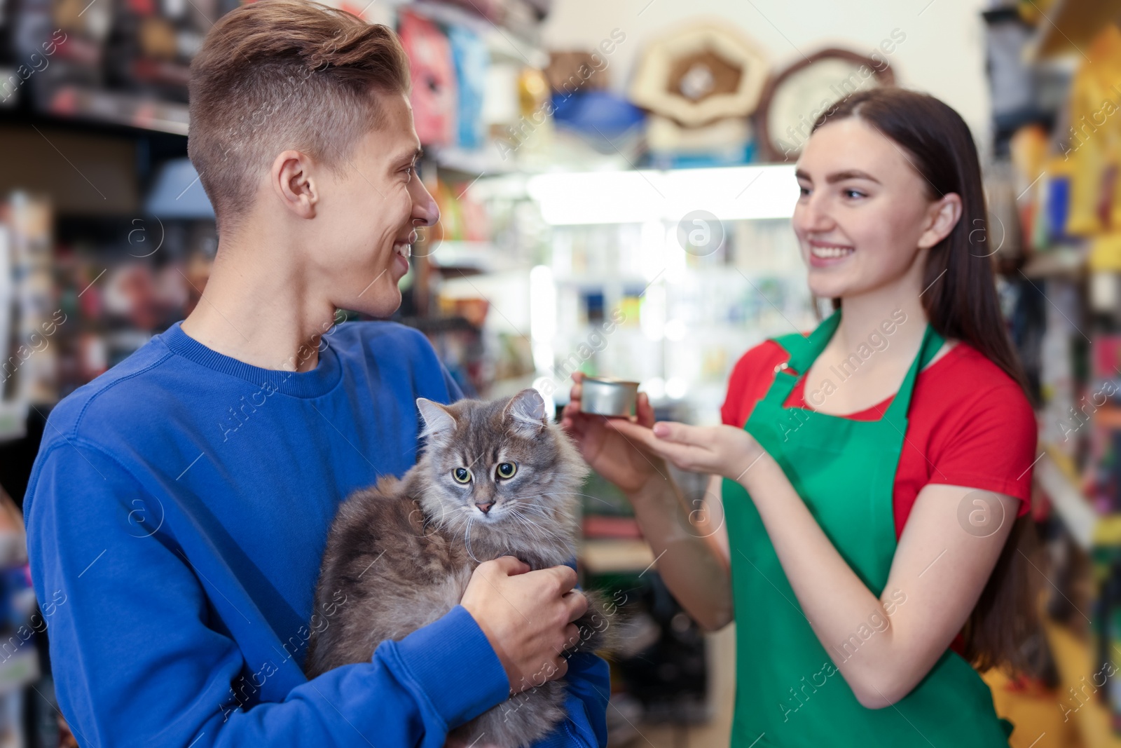 Photo of Pet shop worker recommending food for man's cute cat indoors