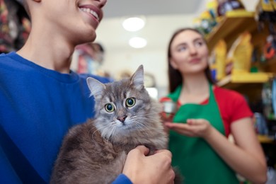 Photo of Pet shop worker recommending food for man's cute cat indoors, selective focus