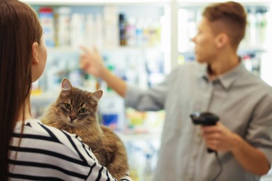 Photo of Cashier recommending cosmetic products to woman with cat in pet shop, selective focus