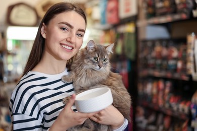 Photo of Woman with her cute cat and feeding bowl in pet shop. Space for text