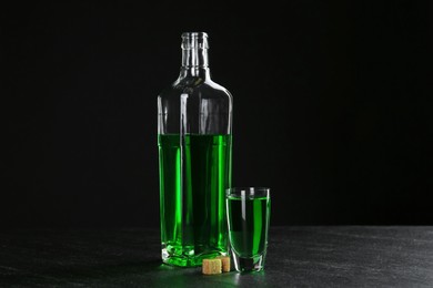 Photo of Absinthe in shot glass, bottle and brown sugar on table against black background