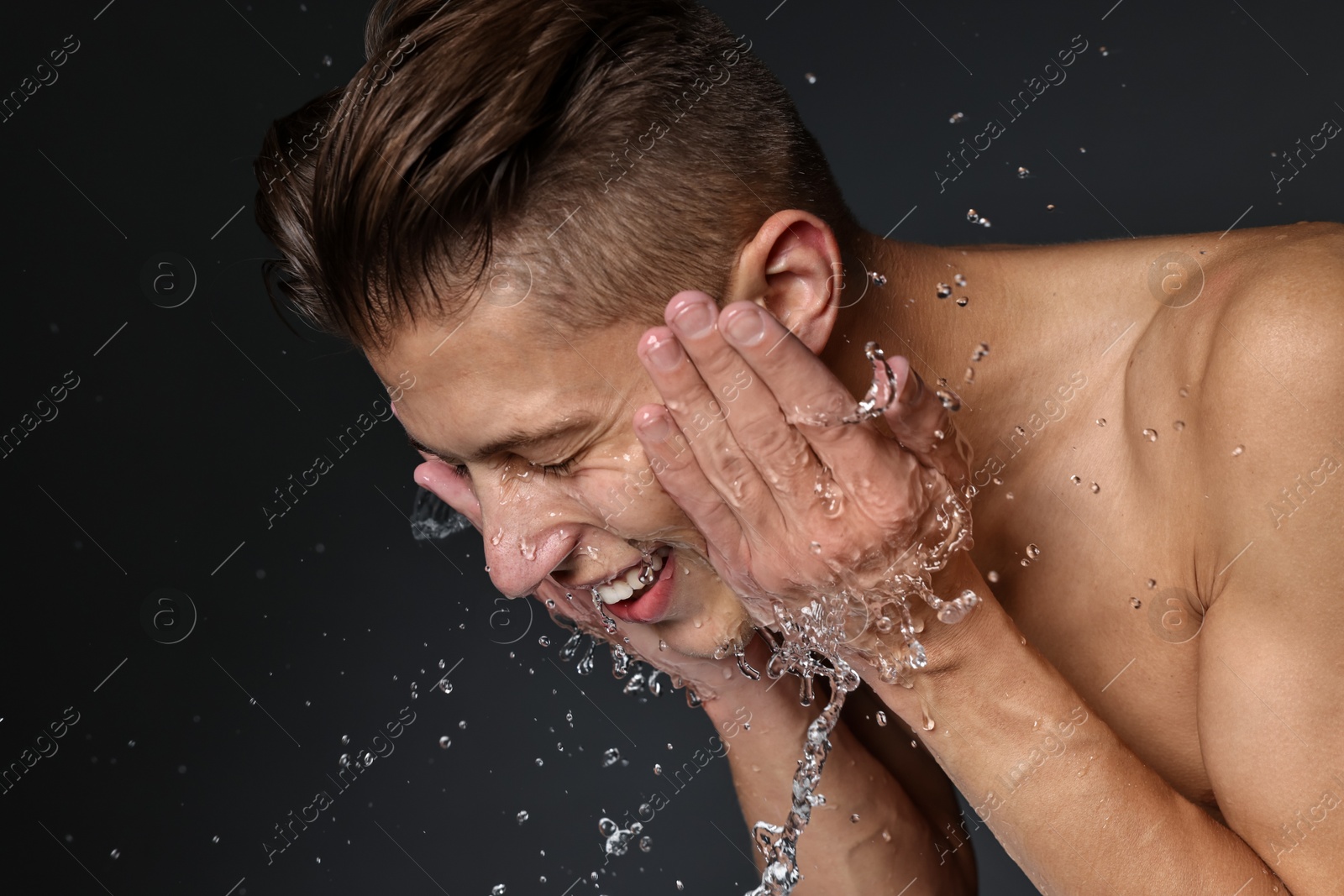 Photo of Smiling man washing his face on black background