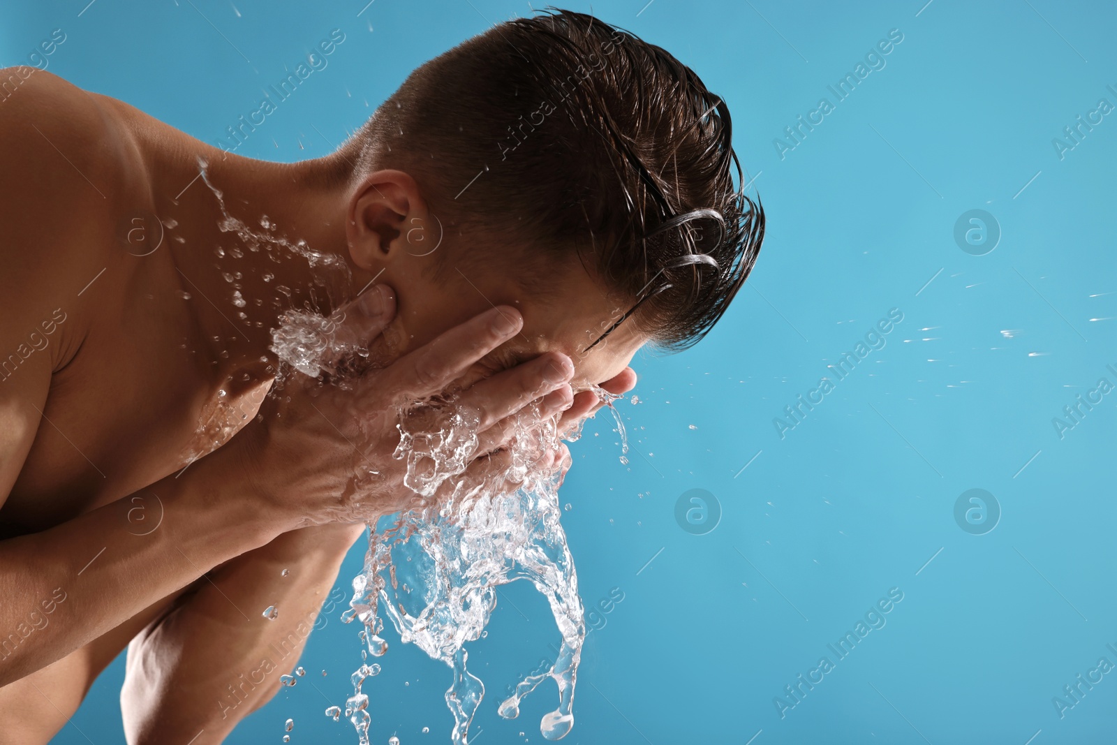 Photo of Man washing his face on blue background. Space for text