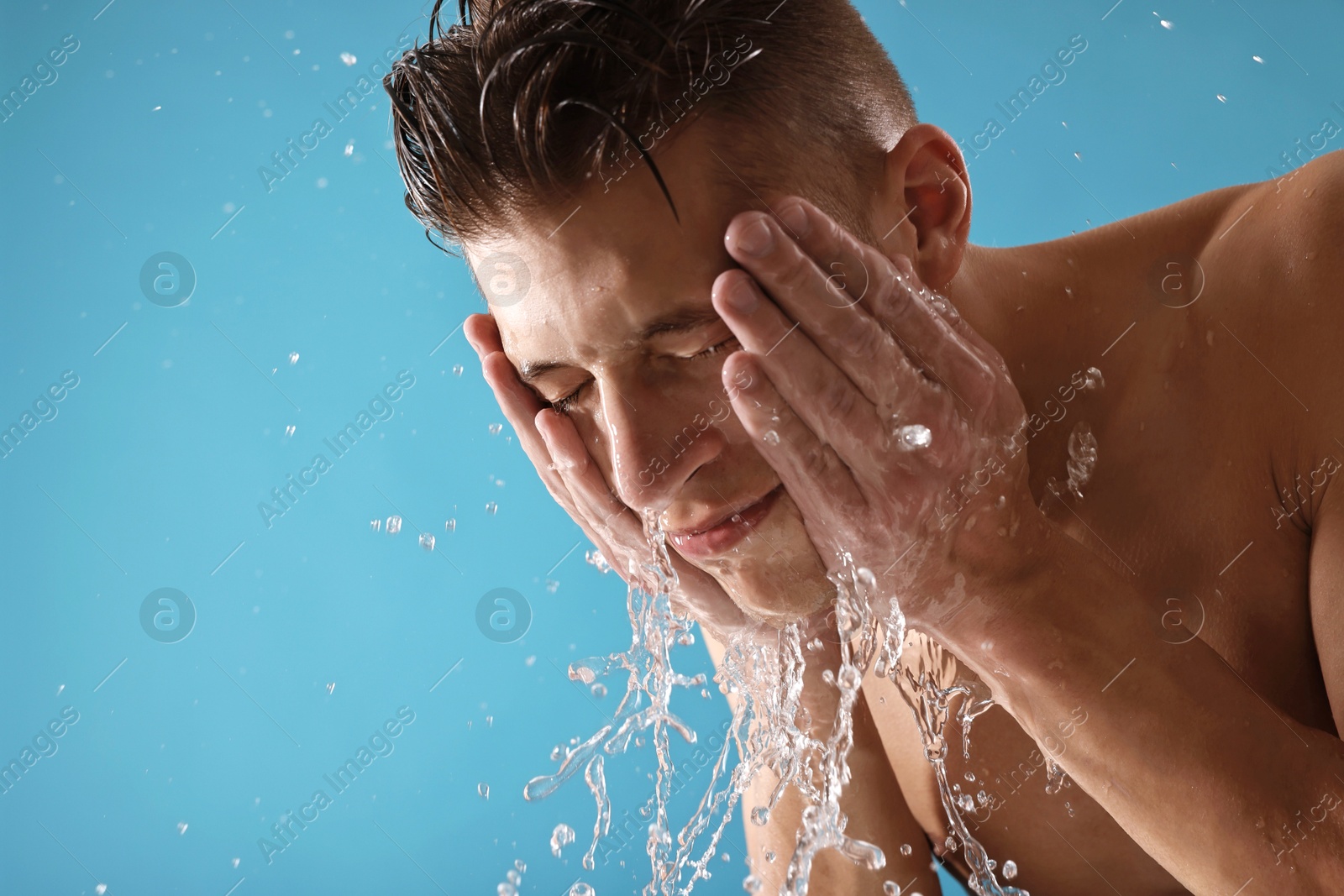 Photo of Handsome man washing his face on blue background. Space for text