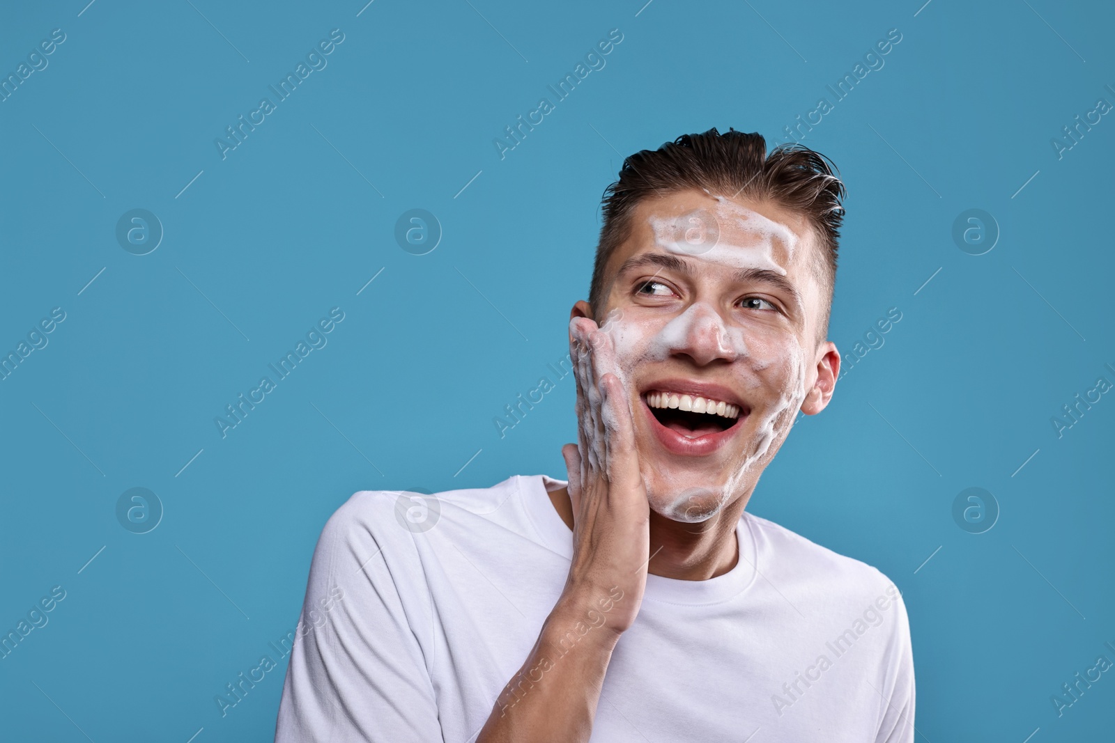 Photo of Smiling man washing his face with cleansing foam on blue background