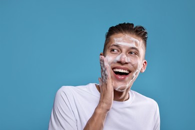 Photo of Smiling man washing his face with cleansing foam on blue background