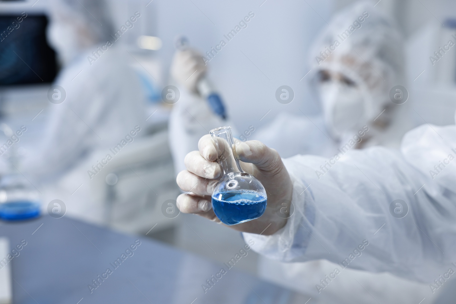 Photo of Scientist holding flask with blue sample in laboratory, closeup