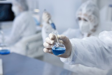 Photo of Scientist holding flask with blue sample in laboratory, closeup