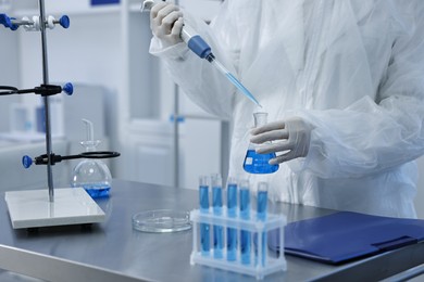 Photo of Scientist dripping blue sample into flask in laboratory, closeup