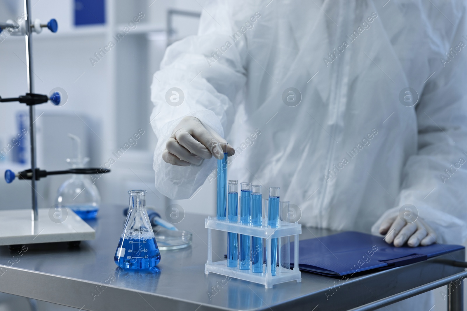 Photo of Scientist taking test tube with blue sample at table in laboratory, closeup