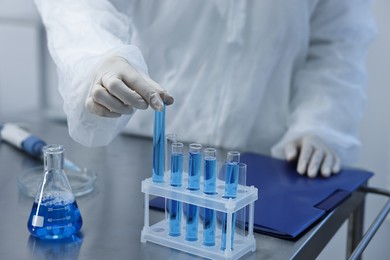 Photo of Scientist taking test tube with blue sample at table in laboratory, closeup