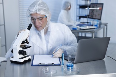 Photo of Scientist with laptop and microscope working at table in laboratory