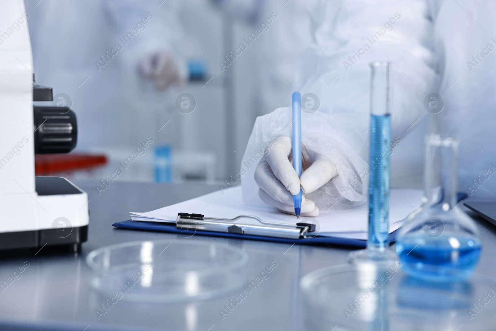 Photo of Scientist with clipboard working at table in laboratory, closeup