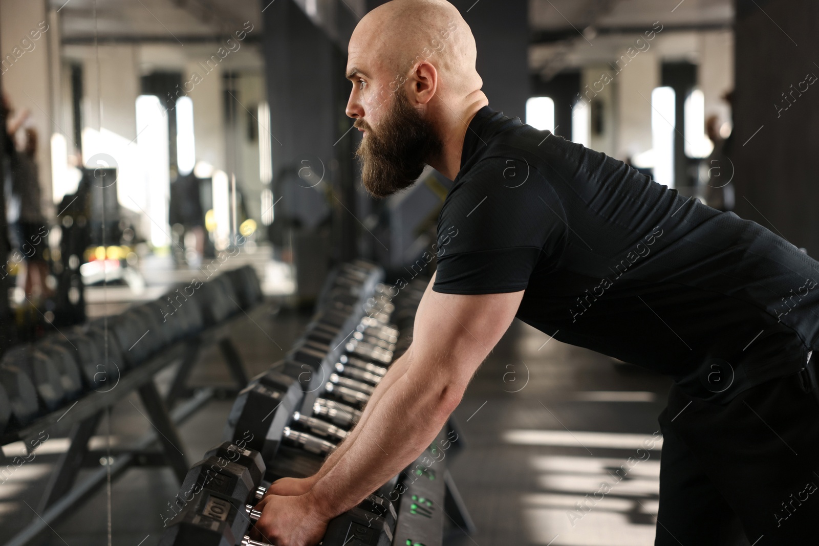 Photo of Sportsman taking dumbbells before crossfit workout in gym