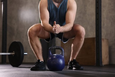 Photo of Sportsman clapping hands with talcum powder before crossfit workout with kettlebell in gym, closeup