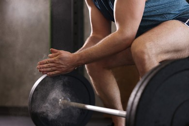 Photo of Sportsman clapping hands with talcum powder before crossfit workout with barbell in gym, closeup