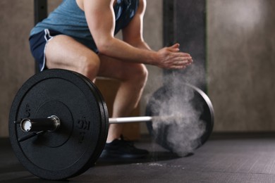 Photo of Sportsman clapping hands with talcum powder before crossfit workout with barbell in gym, closeup