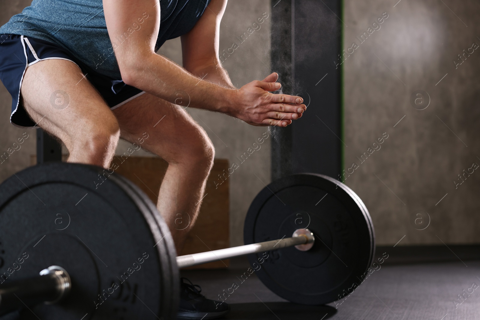 Photo of Sportsman clapping hands with talcum powder before crossfit workout with barbell in gym, closeup