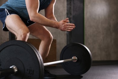 Photo of Sportsman clapping hands with talcum powder before crossfit workout with barbell in gym, closeup