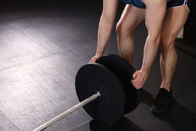 Photo of Sportsman putting weights on barbell before crossfit workout in gym, closeup. Space for text