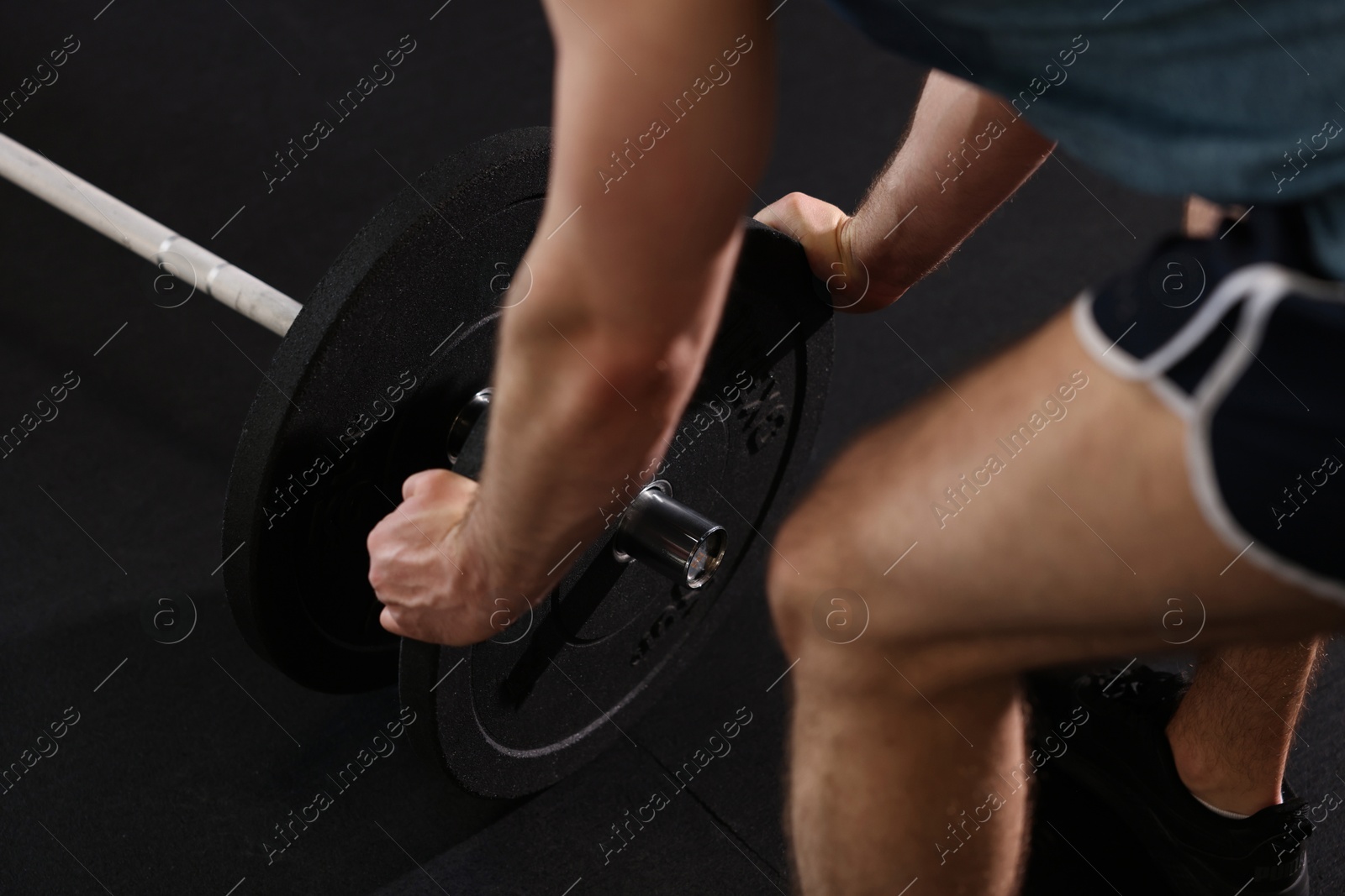 Photo of Sportsman putting weights on barbell before crossfit workout in gym, closeup