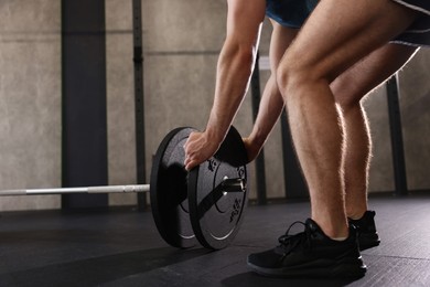 Photo of Sportsman putting weights on barbell before crossfit workout in gym, closeup