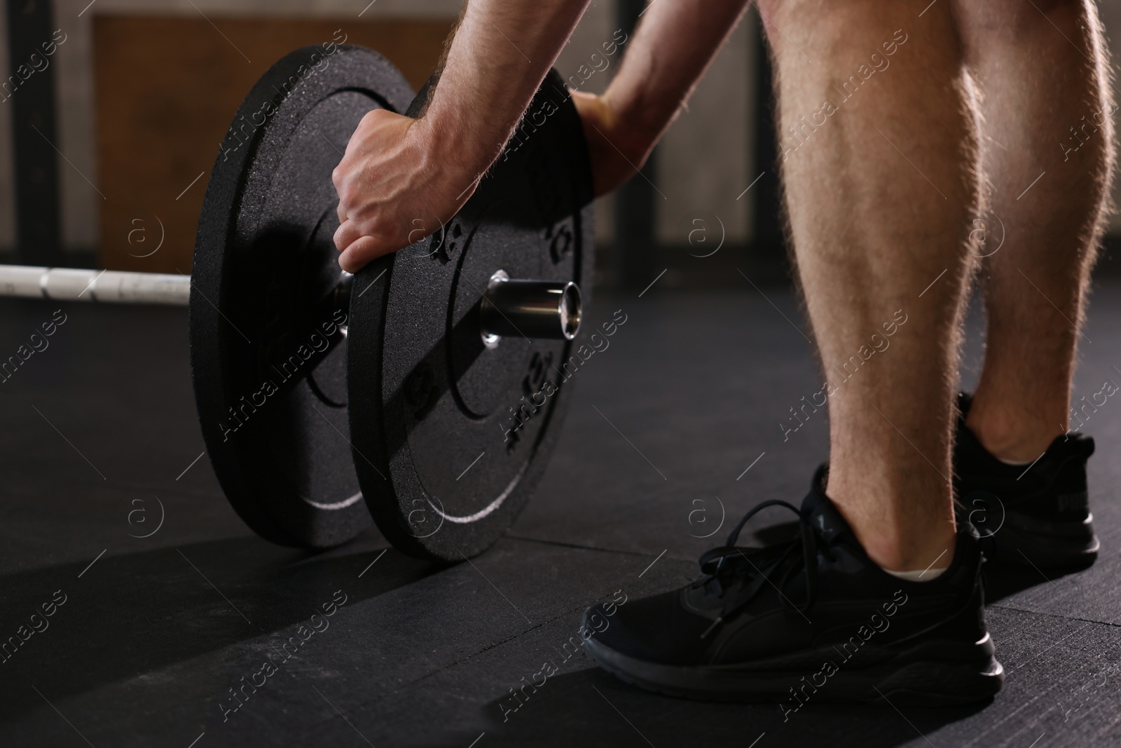 Photo of Sportsman putting weights on barbell before crossfit workout in gym, closeup