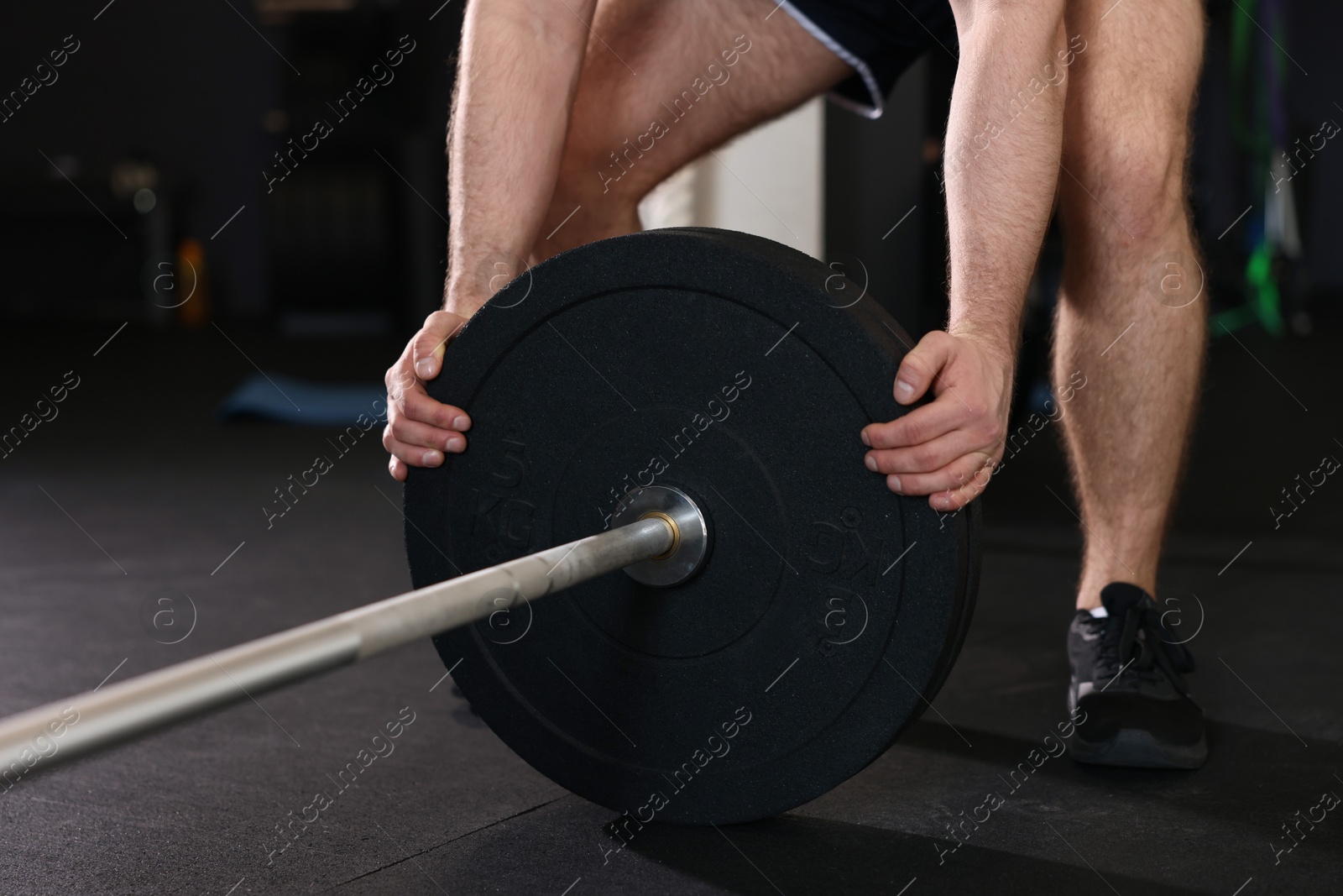 Photo of Sportsman putting weights on barbell before crossfit workout in gym, closeup