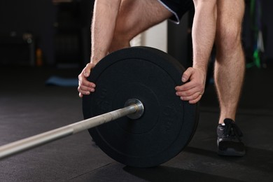 Photo of Sportsman putting weights on barbell before crossfit workout in gym, closeup