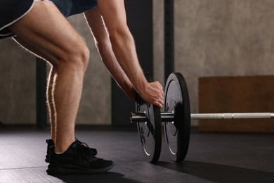 Photo of Sportsman putting weights on barbell before crossfit workout in gym, closeup