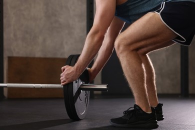 Photo of Sportsman putting weights on barbell before crossfit workout in gym, closeup